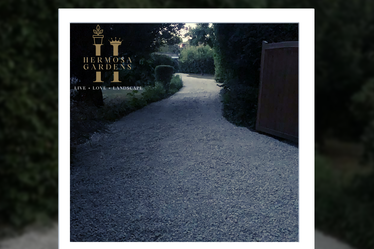 Gravel driveway Gravel pathway leading through greenery, with a gate visible at the end.