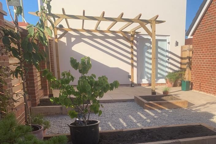 A wooden pergola A wooden pergola casts shadows over a gravel patio, featuring potted plants.