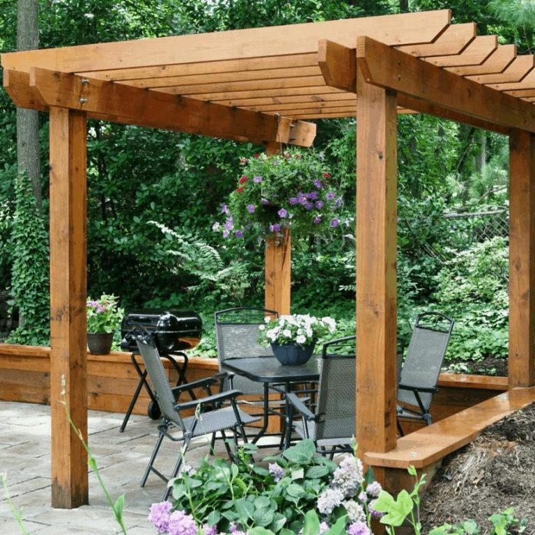 decking, fencing & timber works Wooden pergola with seating area and potted plants in a lush garden setting.