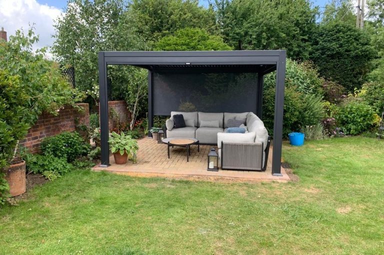 Garden seating area Garden seating area under a black pergola with a grey sofa and table surrounded by greenery.