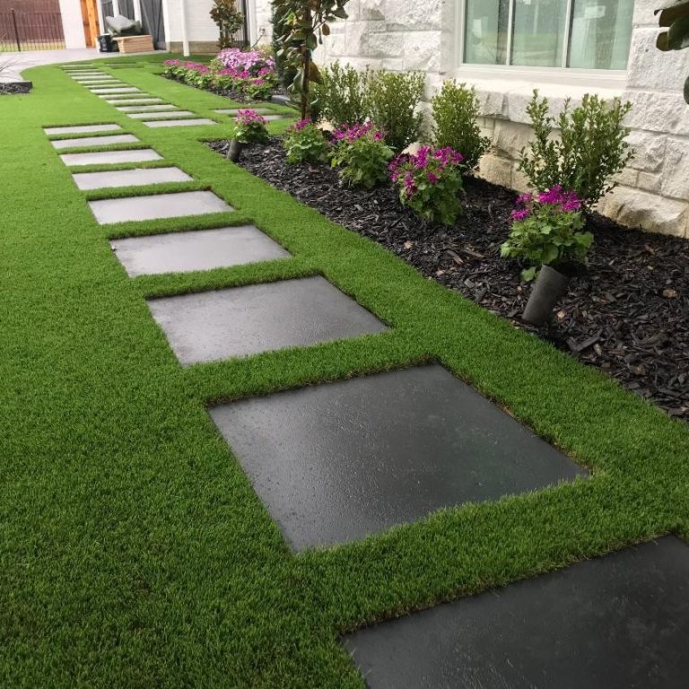 Artificial Grass & Turfing Paved pathway through lush green lawn with flowering plants on either side.
