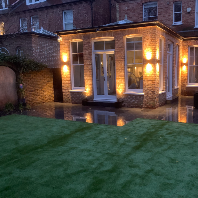 patios & paving A well-lit house exterior with a green lawn and large windows reflecting light.